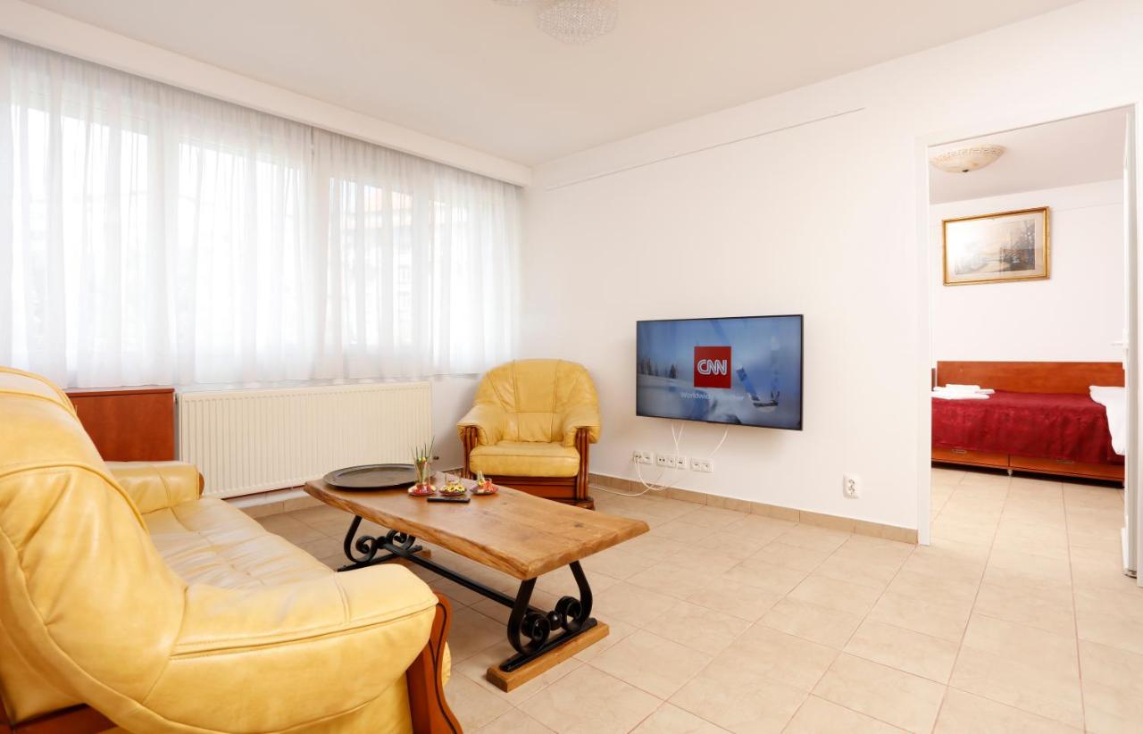 The living room with cream leather sofas, a wooden coffee table and TV, with the bedroom at the back
